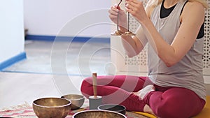 Woman playing on Tibetan singing bowl while sitting on yoga mat. Vintage tonned.