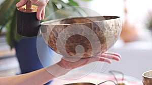 Woman playing on Tibetan singing bowl while sitting on yoga mat. Vintage tonned.