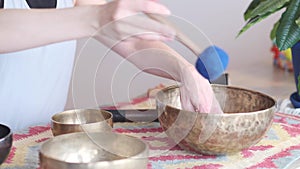 Woman playing on Tibetan singing bowl while sitting on yoga mat. Vintage tonned.