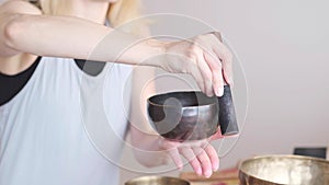 Woman playing on Tibetan singing bowl while sitting on yoga mat. Vintage tonned.