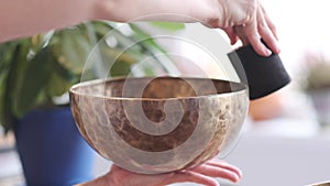 Woman playing on Tibetan singing bowl while sitting on yoga mat. Vintage tonned.