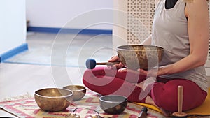 Woman playing on Tibetan singing bowl while sitting on yoga mat. Vintage tonned.