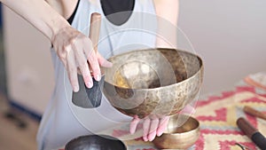 Woman playing on Tibetan singing bowl while sitting on yoga mat. Vintage tonned.