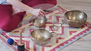 Woman playing on Tibetan singing bowl while sitting on yoga mat. Vintage tonned.