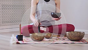 Woman playing on Tibetan singing bowl while sitting on yoga mat. Vintage tonned.