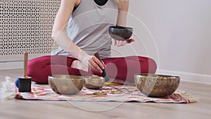 Woman playing on Tibetan singing bowl while sitting on yoga mat. Vintage tonned.