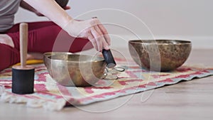 Woman playing on Tibetan singing bowl while sitting on yoga mat. Vintage tonned.