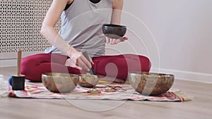 Woman playing on Tibetan singing bowl while sitting on yoga mat. Vintage tonned.