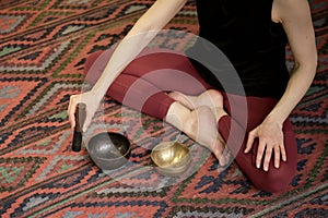 Woman playing on Tibetan singing bowl while sitting on yoga mat. Vintage tonned.