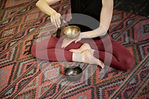 Woman playing on Tibetan singing bowl while sitting on yoga mat. Vintage tonned.