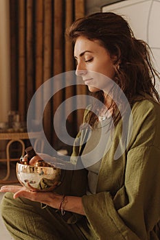 Woman playing on Tibetan singing bowl while sitting on yoga mat. Vintage tonned. Soft focus blurred and noise effect