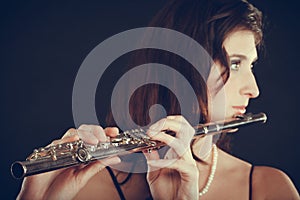 Woman playing transverse flute on black.