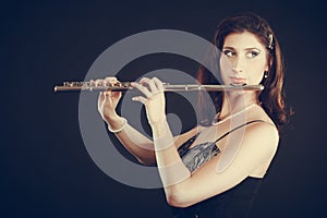 Woman playing transverse flute on black.