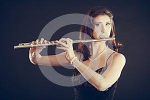 Woman playing transverse flute on black.