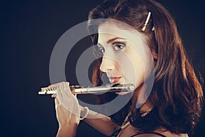 Woman playing transverse flute on black.