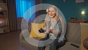 A woman plays a consular game with a game controller while sitting on the couch at home in the evening. A woman often