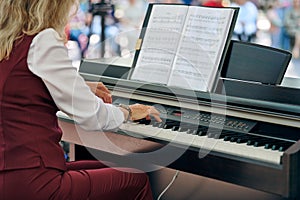 Woman plays electric piano at outdoor music performance, adult female pianist with nimble hands