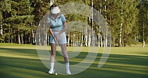 A woman plays golf on a green field in a golf club. Makes a kick to the ball