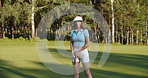 A woman plays golf on a green field in a golf club. Makes a kick to the ball