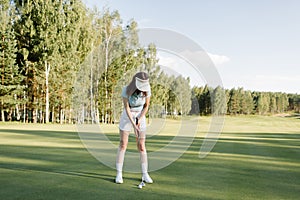 A woman plays golf on a green field in a golf club. Makes a kick to the ball