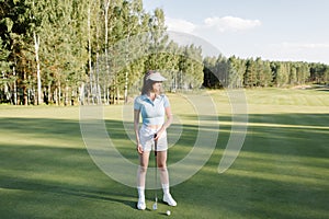 A woman plays golf on a green field in a golf club. Makes a kick to the ball