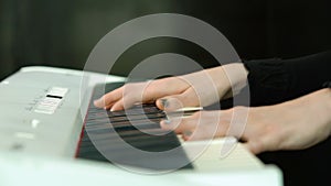 Woman plays by hands on white digital piano, close-up shooting with defocus. Girl is playing by fingers on keyboard or