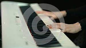 Woman plays by hands on white digital piano, close-up shooting with defocus. Girl is playing by fingers on keyboard or