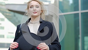 Woman plays with modern black hat moving wide-brimmed chapeau at black coat bottom in street slow motion low angle shot