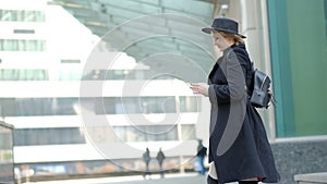 Woman plays with modern black hat moving wide-brimmed chapeau at black coat bottom in street slow motion low angle shot