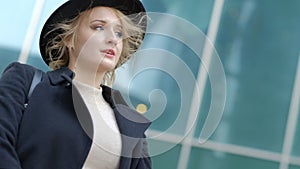 Woman plays with modern black hat moving wide-brimmed chapeau at black coat bottom in street slow motion low angle shot