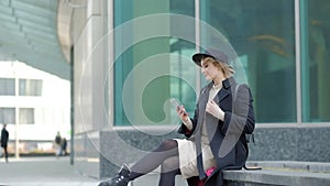 Woman plays with modern black hat moving wide-brimmed chapeau at black coat bottom in street slow motion low angle shot