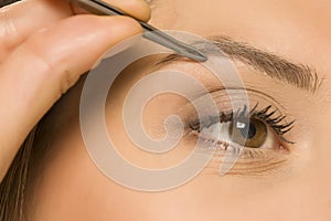 woman plucking her eyebrows with tweezers