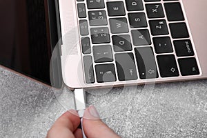 Woman plugging USB cable into laptop port at grey table, closeup