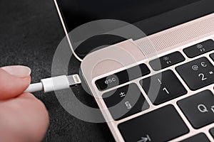 Woman plugging USB cable with lightning connector into laptop port on dark table, closeup