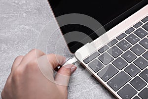 Woman plugging USB cable with type C connector into laptop port at grey table, closeup