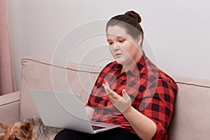 Woman plus size model working online with laptop on her lap, next to a pet dog.