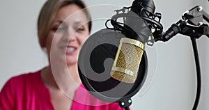 Woman podcaster sits at table and speaks into microphone on tripod and shares information