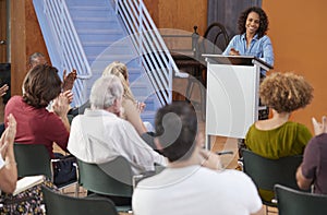 Woman At Podium Chairing Neighborhood Meeting In Community Centre