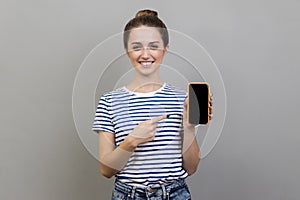 Woman pointing at cell phone and smiling at camera, showing telephone, copy space.