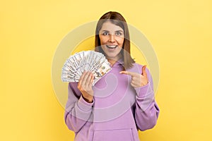Woman pointing at dollar banknotes in her hand, having positive expression, big profit.