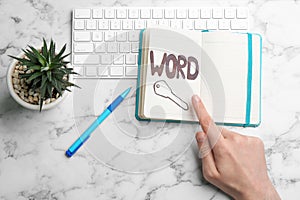 Woman pointing at drawn key in notebook, top view. Keyword concept