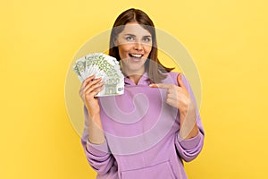 Woman pointing at euro banknotes in her hand, having optimistic positive expression, big profit.