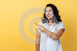 Woman pointing finger away with toothy smile, wondering about empty space for your advertisement.