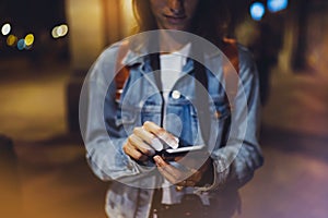 Woman pointing finger on blank screen smartphone on background bokeh light in night atmospheric city, blogger hipster using