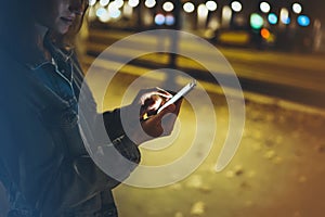 Woman pointing finger on screen smartphone on background illumination bokeh light in night atmospheric city, hipster using in hand