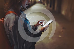 Woman pointing finger on screen smartphone on background illumination bokeh light in night atmospheric city, hipster using in hand