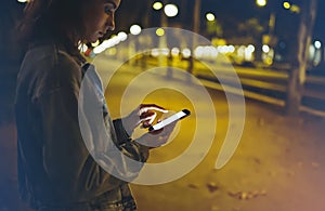 Woman pointing finger on screen smartphone on background illumination bokeh light in night atmospheric city, hipster using in hand