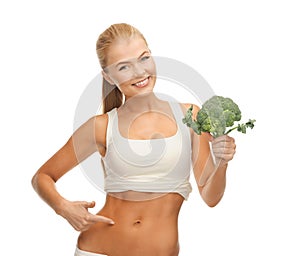 Woman pointing at her abs and holding broccoli