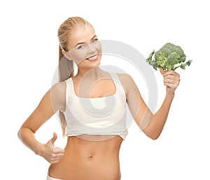 Woman pointing at her abs and holding broccoli