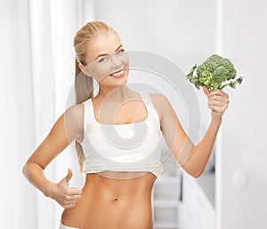 Woman pointing at her abs and holding broccoli